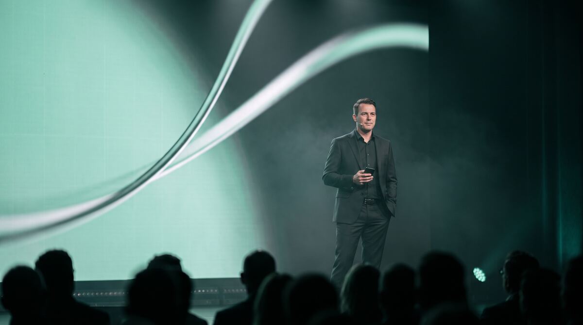 A presenter on a lit stage in front of an audience, playing in the Cliqer Live player